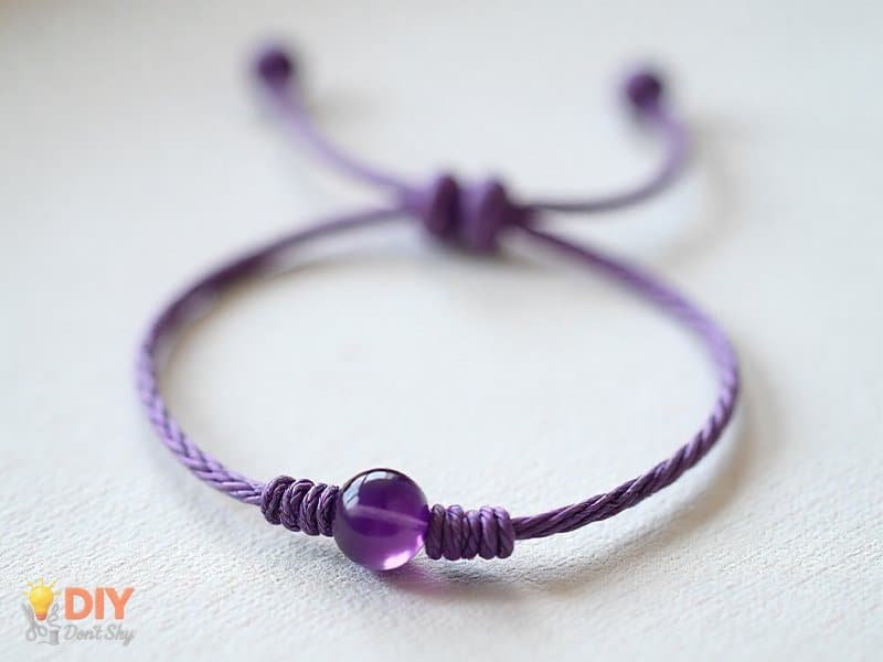 Silk cord bracelet with a single amethyst birthstone bead and neat knots.