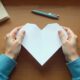 Student folding a plain sheet of paper into a heart shape on a desk.