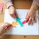 Hands making colorful paper arrows on a wooden table with scissors, glue, and markers for a fun DIY craft project.