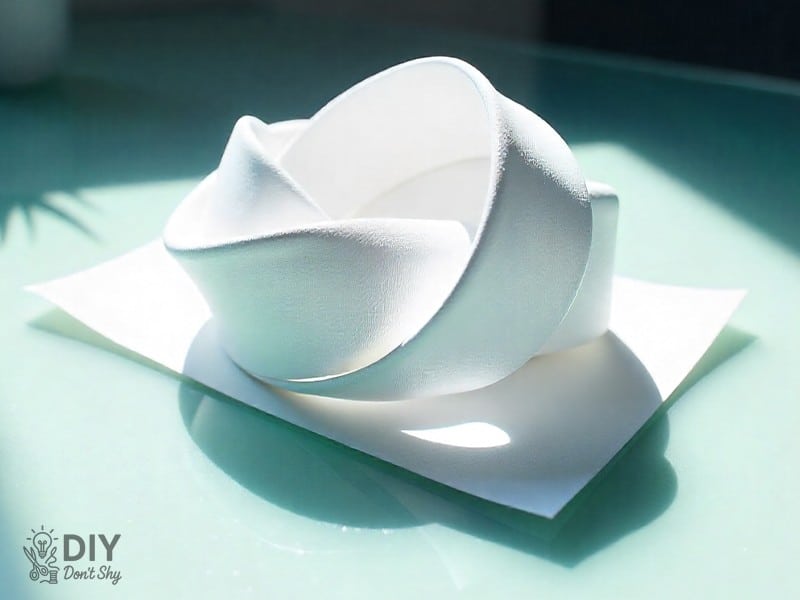 Flattened paper knot forming a pentagon base for a paper star craft.