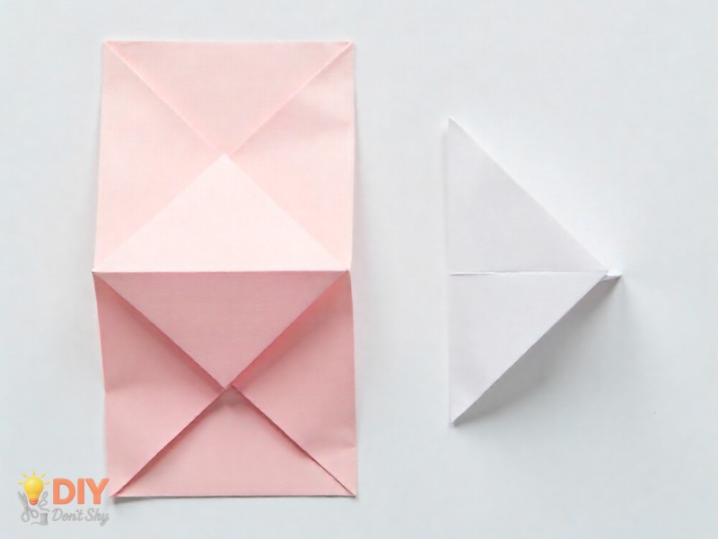 Origami paper folded into a large and smaller triangle step on white background.