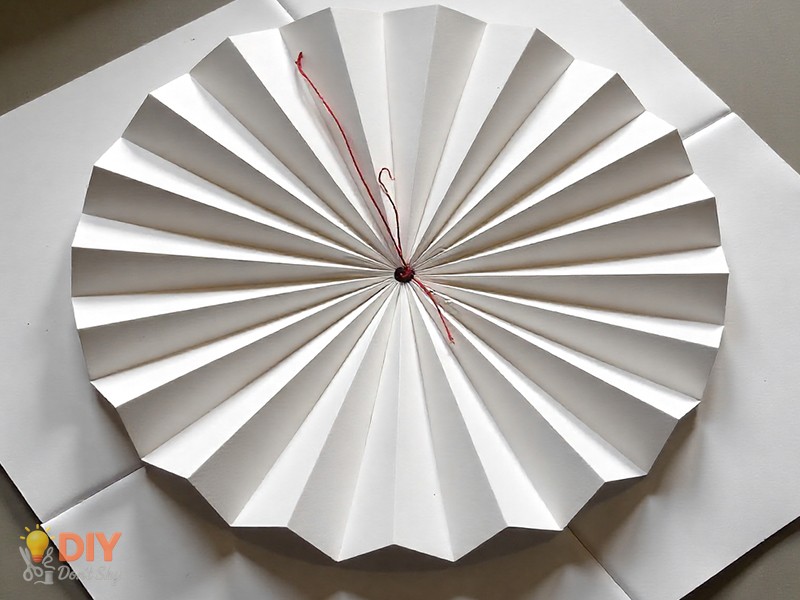 Pleated paper folded into a circular shape with thread through the center to create a button without glue.