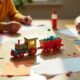 Realistic homemade paper train craft in progress with hands cutting and gluing paper on a family table.